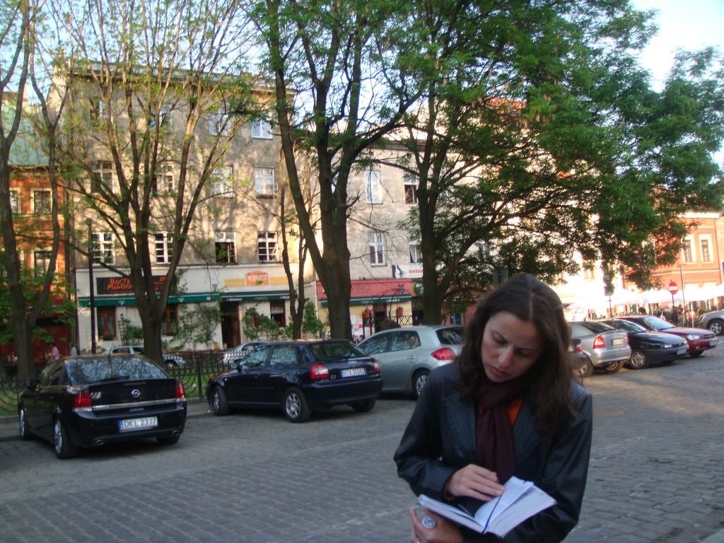 Raquel, autora do blog, parada em uma rua consultando um guia de viagem em Cracóvia, Polônia