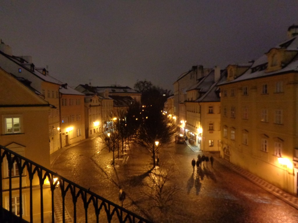 Foto noturna do bairro de Malá Strana em Praga, com iluminação amarelada valorizando a arquitetura dos prédios
