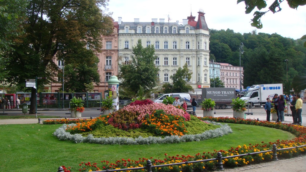 Jardim bem cuidado com muitas flores, ao fundo prédios históricos na cidade de Karlovy Vary