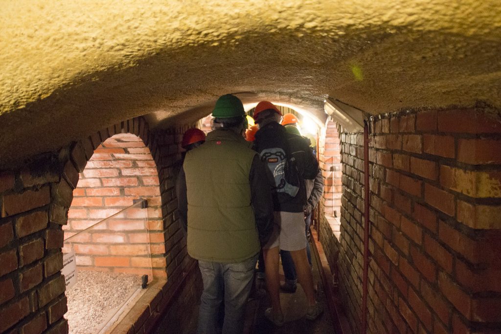 Pessoas andando com capacete em um corredor estreito, baixo e úmido da cidade subterrânea de Pilsen