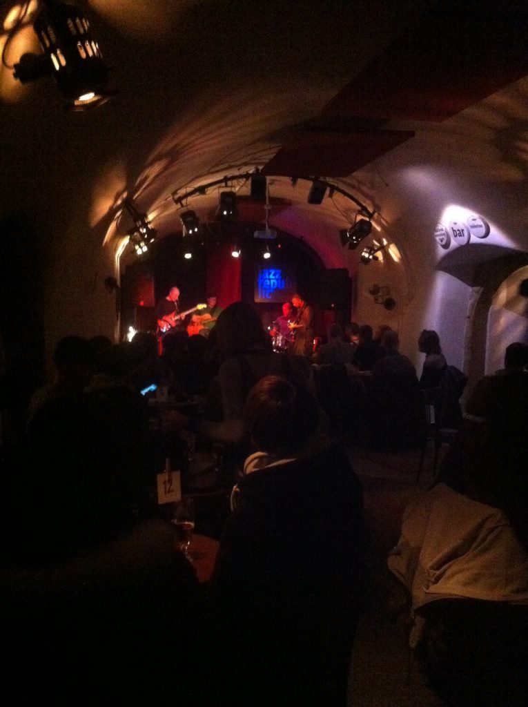 Club de jazz em Praga com banda se apresentando no palco e várias pessoas sentadas na mesa na frente da banda