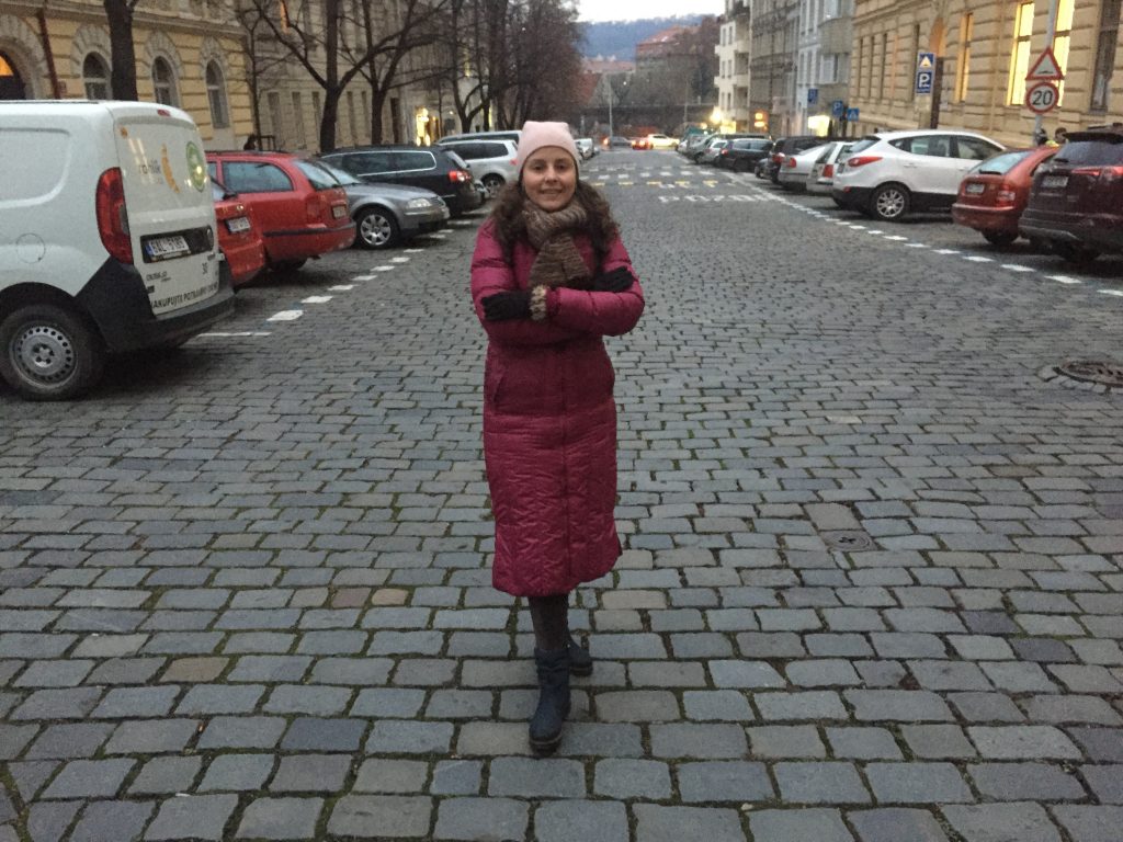 Foto da Raquel, autora do blog, bem no meio de uma rua em Praga, vestida com casaco mais pesado de inverno