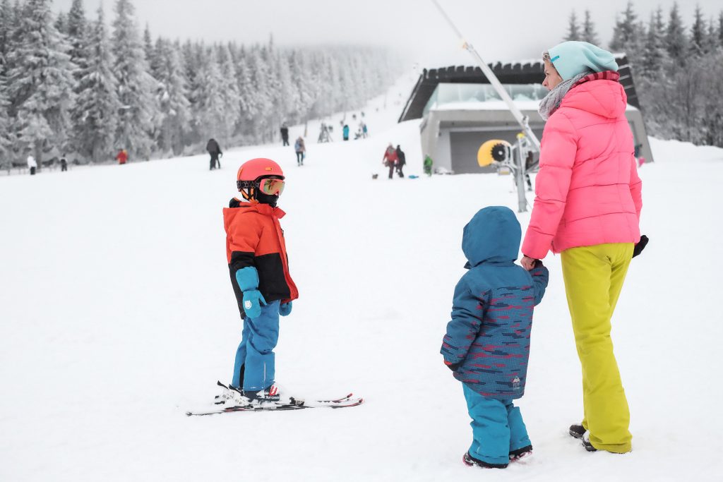 Crianças e adulto acompanhando um dia de esqui em uma montanha branquinha de neve