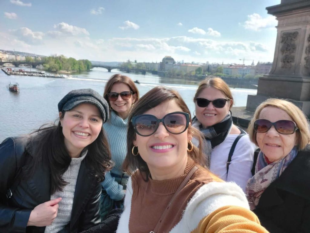 A cliente e viajante, Ana Teresa, fazendo uma selfie de um passeio em Praga. Na foto, aparecem eu e mais três mulheres da família dela. Ao fundo, o rio Moldava de Praga.