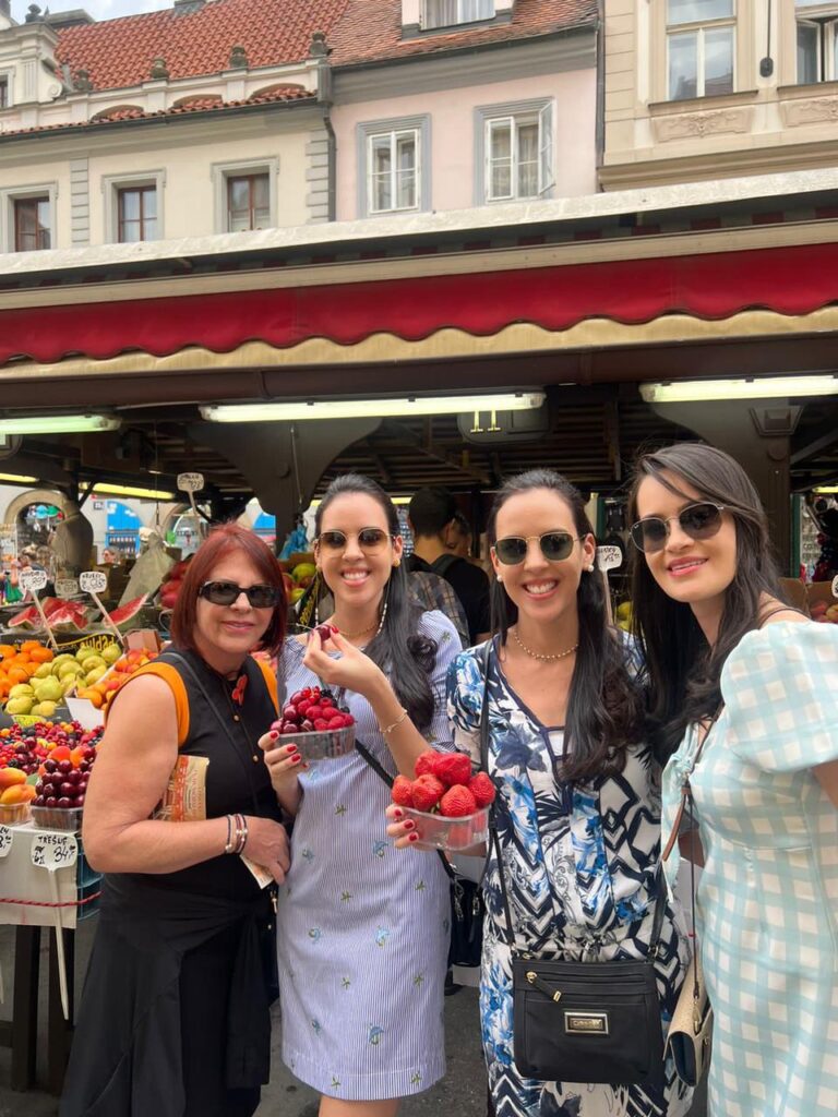 Quatro mulheres juntas sorrindo e segurando uma caixa de morangos numa feira de rua em Praga em Julho de 2022