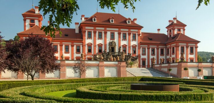 Fachada barroca de um palacio majestoso com um jardim ornamentado à frente do palacio em Praga